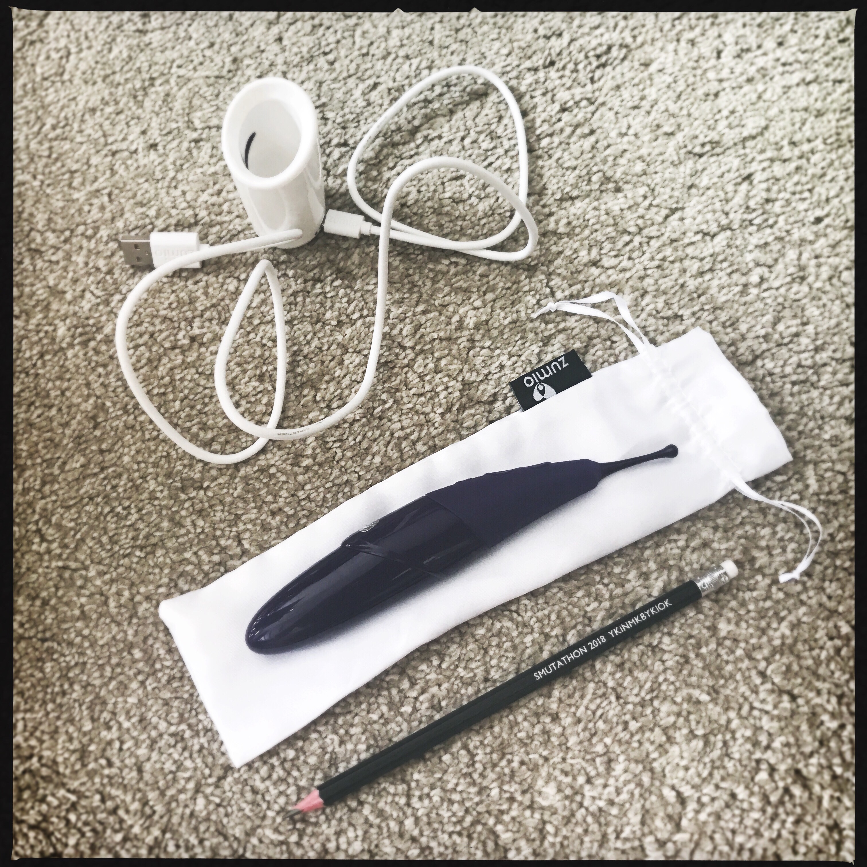 A photo showing that the Zumio sex toy is about the length of a pencil. It is lying on its white fabric case with that charging station and cable next to it