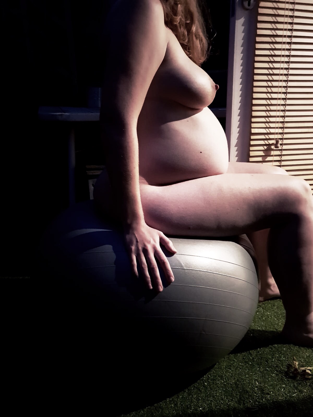 My 34 week pregnant self still naked on the grey exercise ball, this time in profile and facing towards the light to emphasise my growing bump