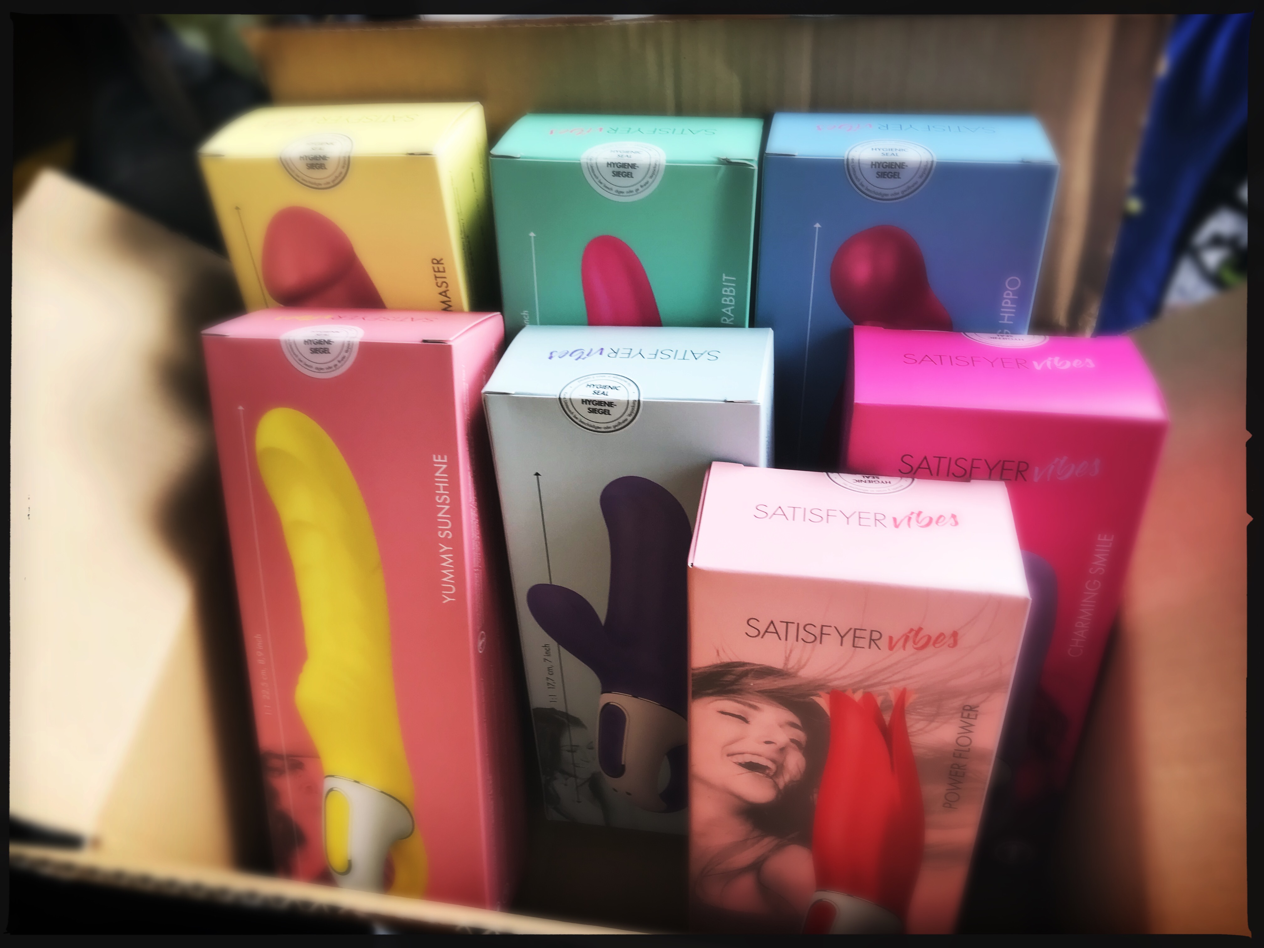 A photo of a cardboard box filled with colourful boxes of vibrators